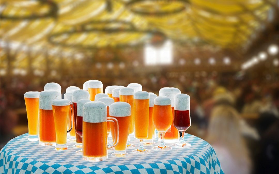Mugs and glasses of amber and golden Oktoberfest beer on a blue and white checked table in a beer tent