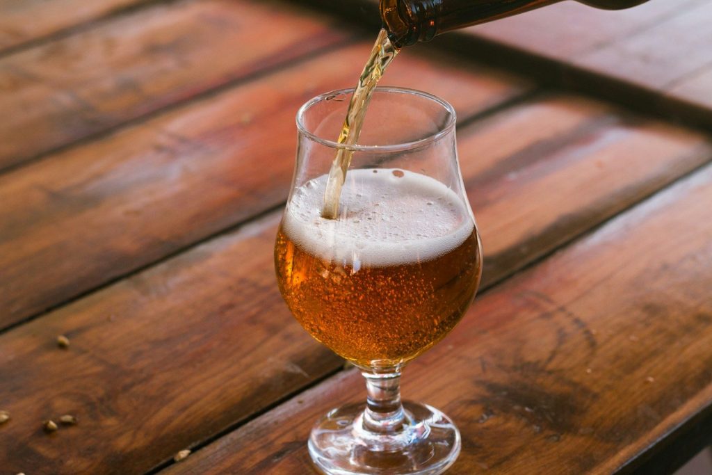Beer being poured from a bottle into a tulip glass on a wooden table